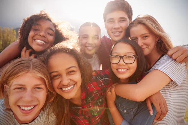 The image shows a group of young people, male and female hugging, smiling and looking at the camera.