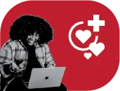 A woman smiling as she types on a laptop with a red background behind her with heart and plus sign symbols.
