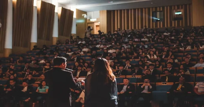 A man and a woman addressing an audience in an auditorium. 