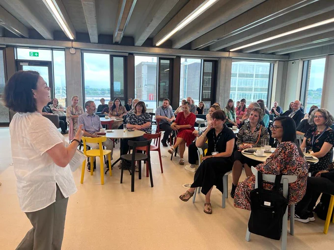 Woman stood addressing a room of people 