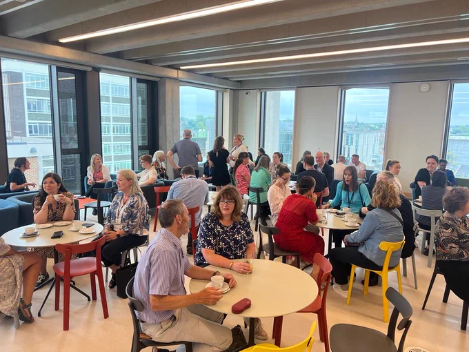 A room of people sat around tables talking 