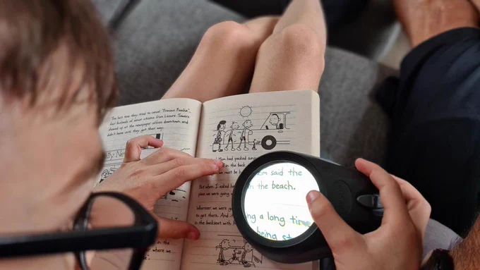 Boy reading his book using a low vision aid. 