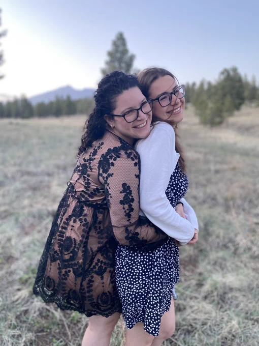 Lexi hugs Eva from behind in front of the San Francisco Peaks. They are both dressed up for a gala.