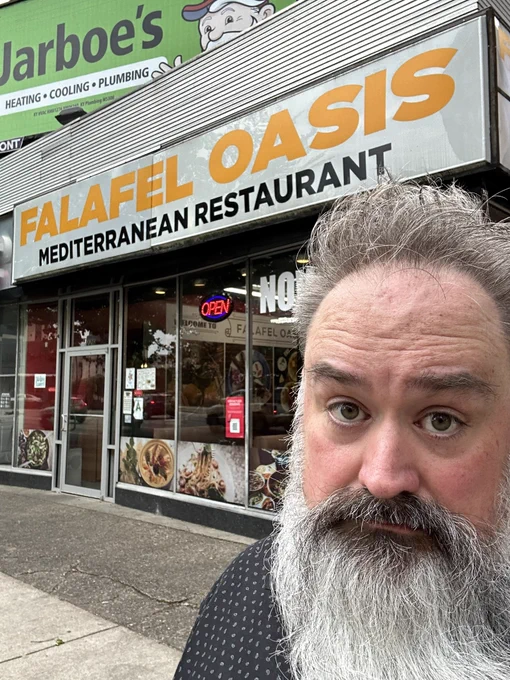 Bryce standing outside a dive restaurant called falafel oasis