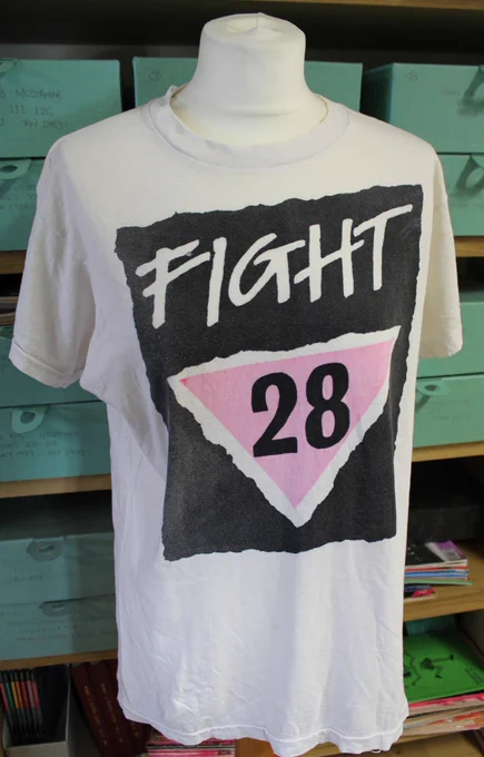 A t-shirt on a mannequin that says 'fight 28' on it. The '28' is inside an upside-down pink triangle.

