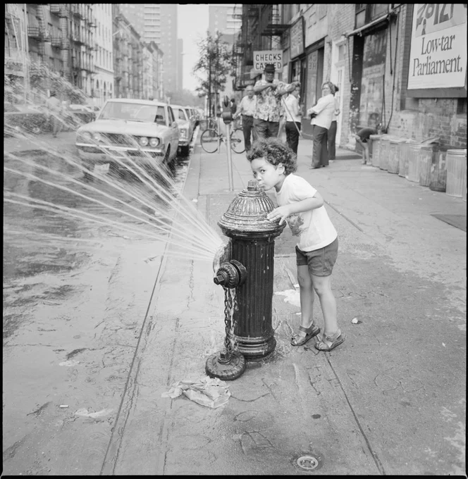 A child kisses the top of a spraying fire hydrant.  