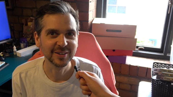 Lewis is looking at the camera with a tiny microphone by his mouth about to say something.