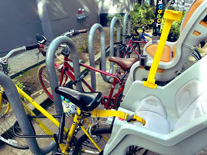 Red bike and yellow bike locked side by side at bike rack. Both have child seats on the rear rack.