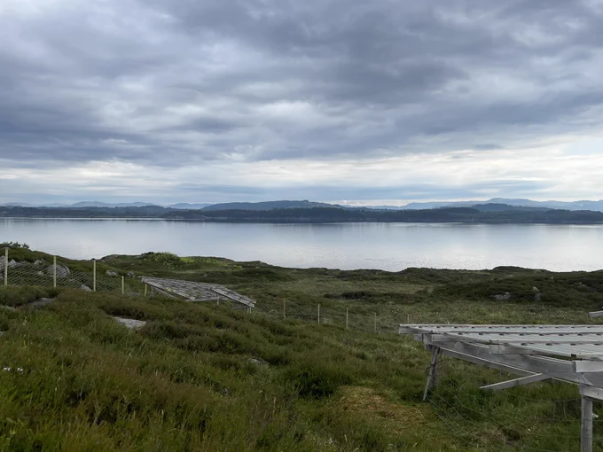 Dramatic stormy skies over a calm bay with very short rainout shelters and a heathland in the foreground.