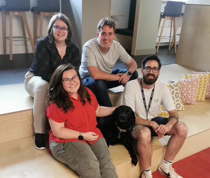 The accessibility team sat in the Nexer Digital office. Included is Emma, Molly, Chris, Bella (Molly's guidedog) and Danny 