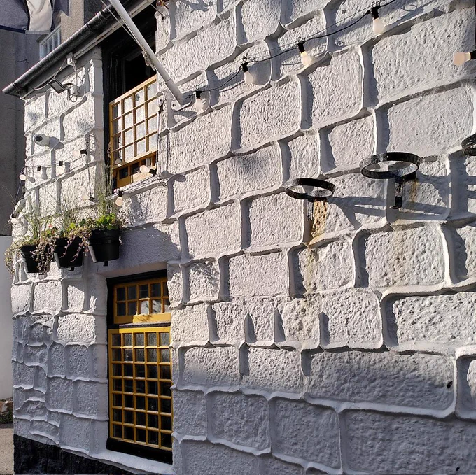 A whitewashed pub wall, with mortar standing proud of the stones.
