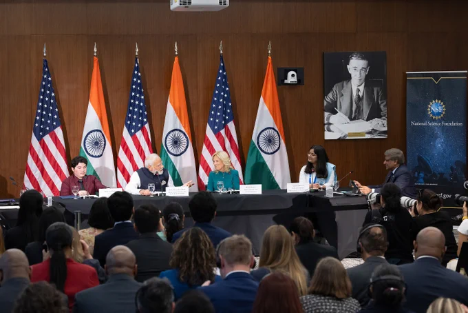 In front of a crowd gathered at NSF headquarters, Indian Prime Minister Narendra Modi, First Lady Dr. Jill Biden, and NSF Director Sethuraman Panchanathan, among others, sit at a long table in front of the American and Indian flags.