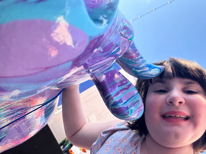 A young girl smiles with a CowParade cow while taking a selfie.