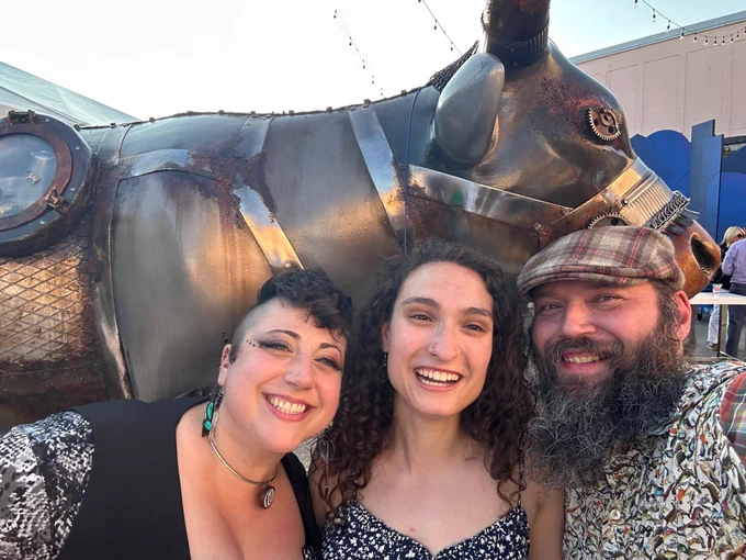 Three attendees at the CowParade launch party smile while taking a selfie with one of the CowParade New England cows.