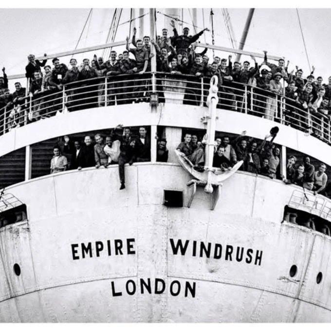 Black and white photograph of an Empire Windrush ship arriving. People are waving who are on board.