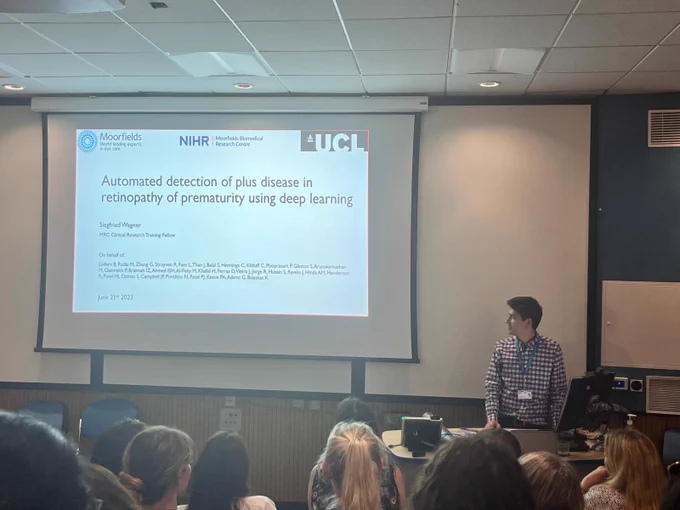 Siegfried in lecture theatre with a slide up and title of the paper ‘automated detection of plus disease in retinopathy of prematurity using deep learning’