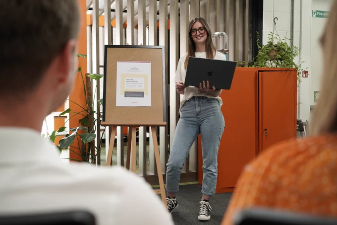 Martika delivering this weeks UX presentation on Hierarchy - stood in the Epix Studio next to an easel with this weeks poster on it, as Epix team members look on and listen
