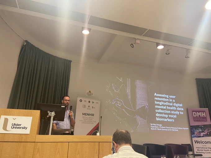 A photo of Philip Donaghy delivering a presentation on 'Assessing user retention in a longitudinal digital mental health data collection study to develop vocal biomarkers'.