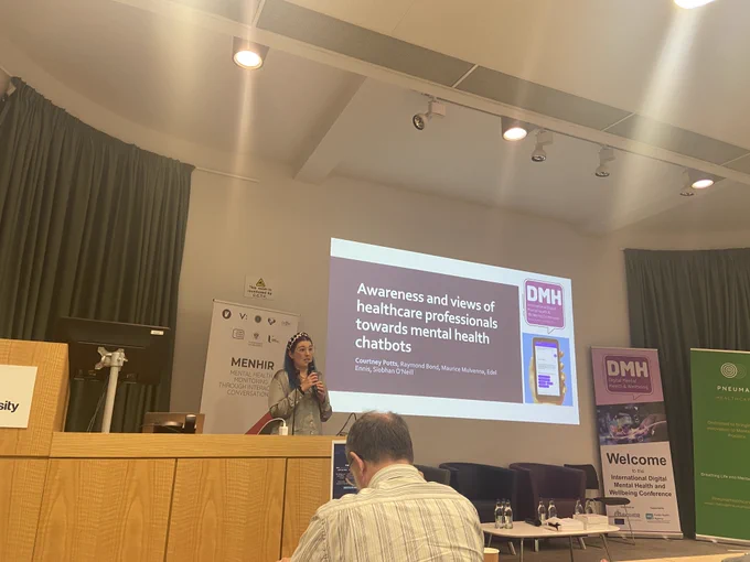 A photo of Courtney Potts delivering a presentation on 'Awareness and views of healthcare professionals towards mental health chatbots'.