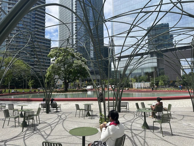 People sit under a wire pavilion next to a large pond. 