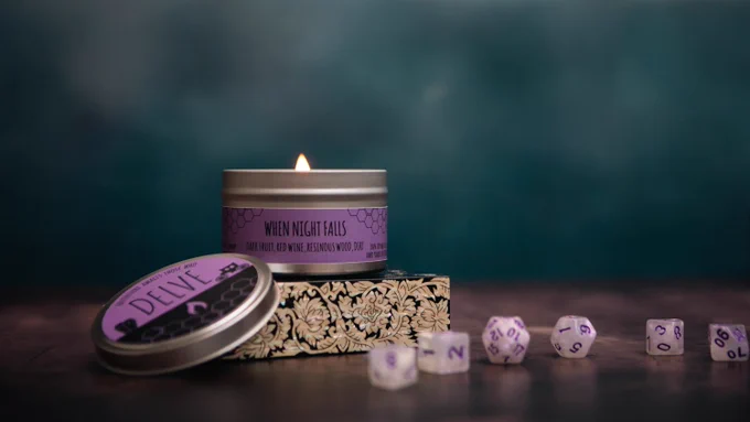 A lit candle with a purple label reading "When Night Falls." The foreground has a white set of polyhedral dice.