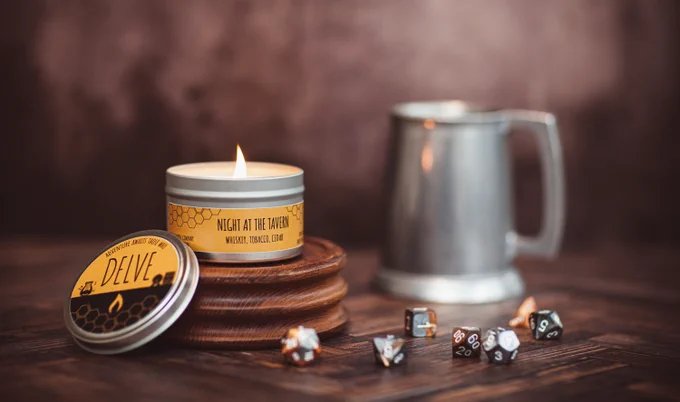 A lit candle with an orange label reading "Night at the Tavern." The foreground has a metallic colored set of polyhedral dice.