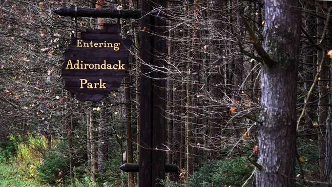 A wooden sign hanging from a tree that says "Entering Adirondack Park." Photo by Connor Ludwin