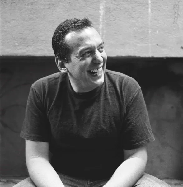 VD: Christos smiling while sitting outside against a brick background.