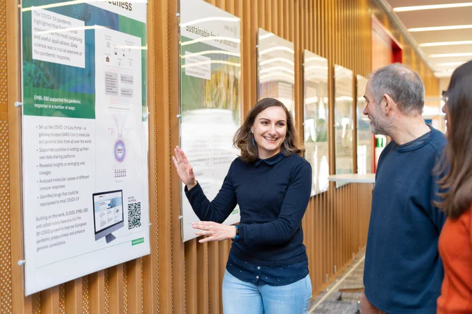A smiling delegate points to her scientific poster 