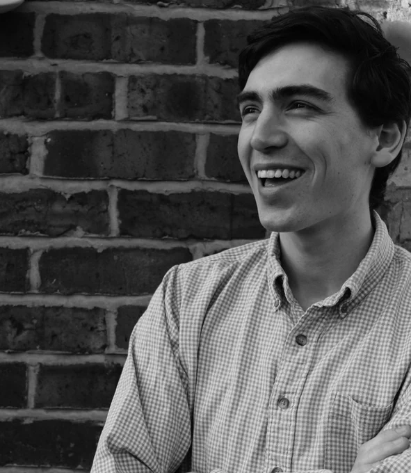 A black and white headshot of Charlie Perry, wearing a checkered shirt, smiling off camera.