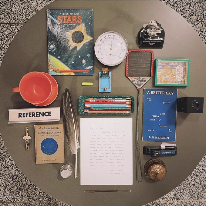 A letter on a round table surrounded by small office items from the mid-20th century in the style of a Wes Anderson film