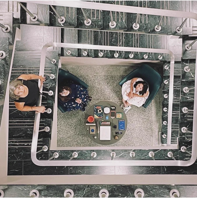 A top-down view of the table with the letter on it, at the bottom of a spiral green marble staircase. Three librarians look up at the camera.