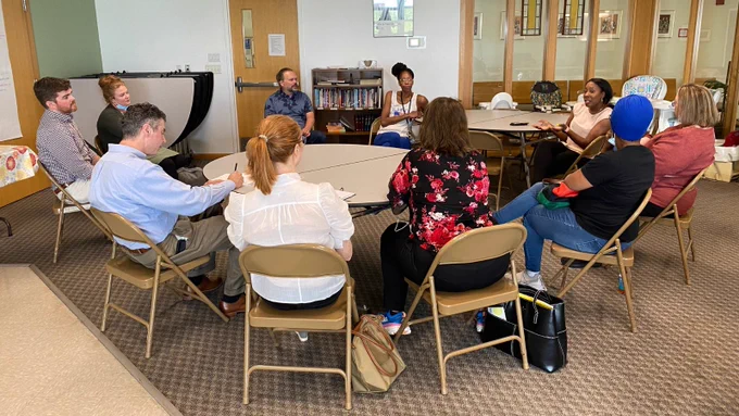 Ten people sit at a table having a discussion. 