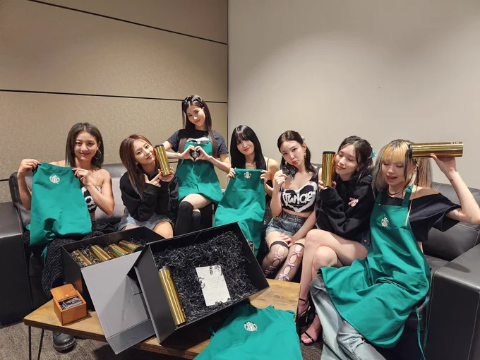 Seven members of the K-pop group Twice posing with Starbucks merchandise.