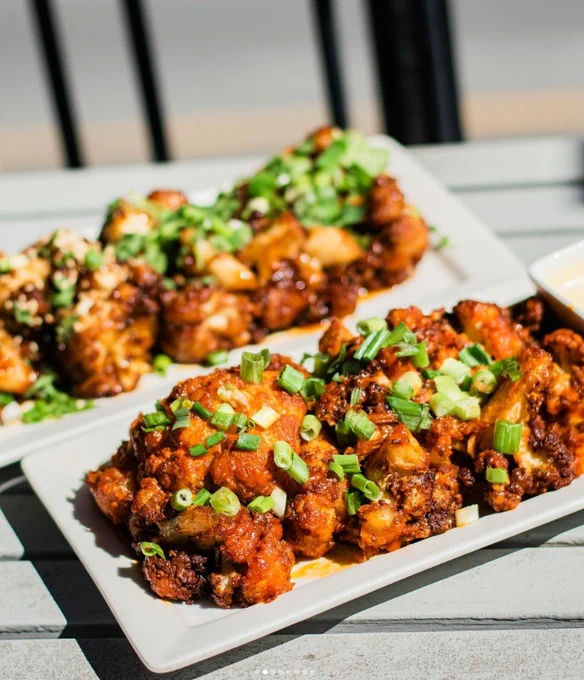 Image of two rectangle plates of cauliflower wings topped will scallions.