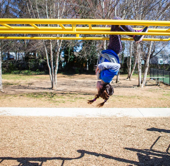 A photo of a student hanging upside down on the monkey bars at a school playground.