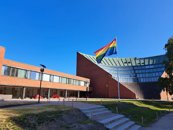 Pride flag in front, the Undergraduate Centre building behind with blue skies.