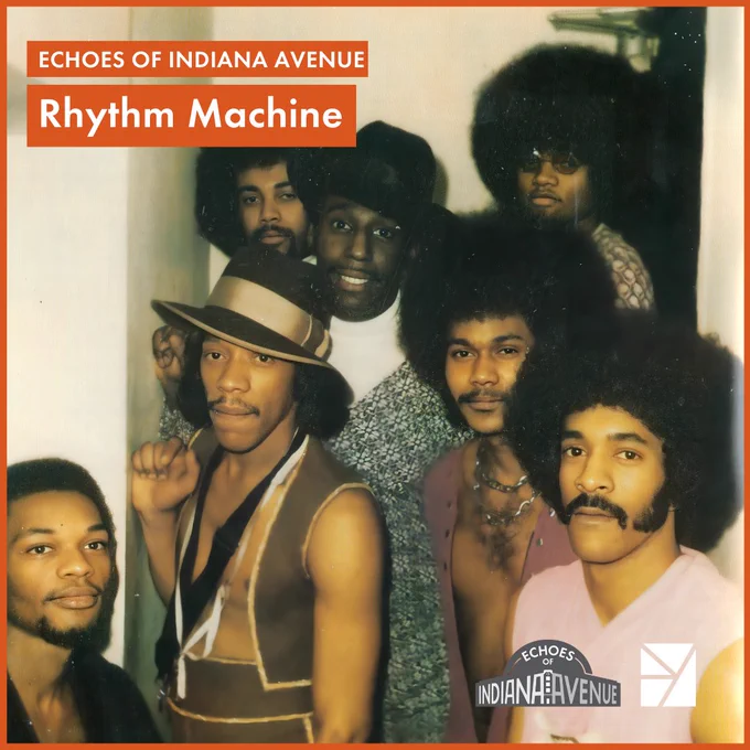 Seven men standing in a hallway staircase wearing vintage clothes. Four of the men have afros and two are wearing fancy hats. Text in the top left corner read: Echoes of Indiana Avenue Rhythm Machine.