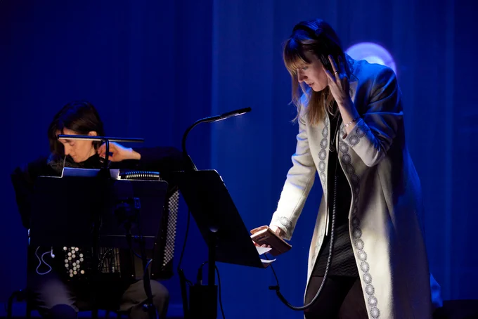 A composer with headphones looking at a score, next to a performer