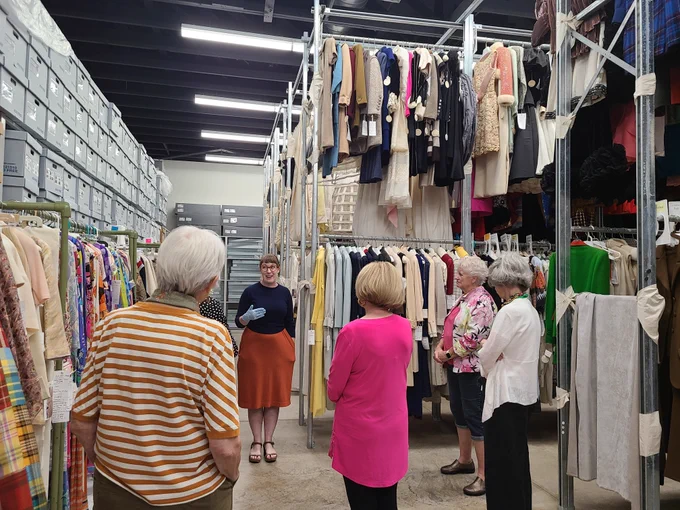 A group of senior adults stand inside the Texas Fashion Collection. A collection staff member is speaking to them.