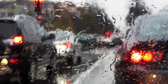 View from the driver's seat inside a vehicle out the windshield. Weather is rainy and there is traffic. 