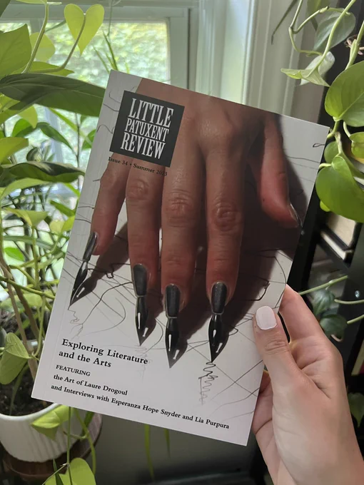 A hand holds a copy of Little Patuxent Review ‘s latest issue in front of green plants. The cover of the issue features art by Laure Drogoul—an image from a performance art piece where a hand is transformed into a fountain pen. Each fingertip has a pen tip and ink attached to the nail. Scribbles fill the white background.