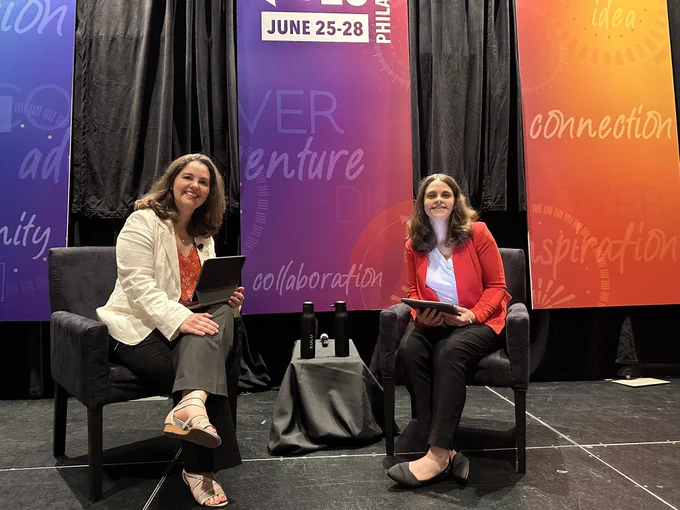 Jordyn and Janette seated on a stage in conversation. Janette is asking questions and Jordyn is responding via typing on iPad.