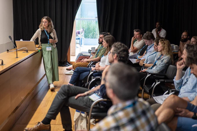 Photograph of MEDEA Finalist Screening Session - Elena Riedlinger preseing her entry ''Stolpersteine NRW'' in front of room full of attendees.