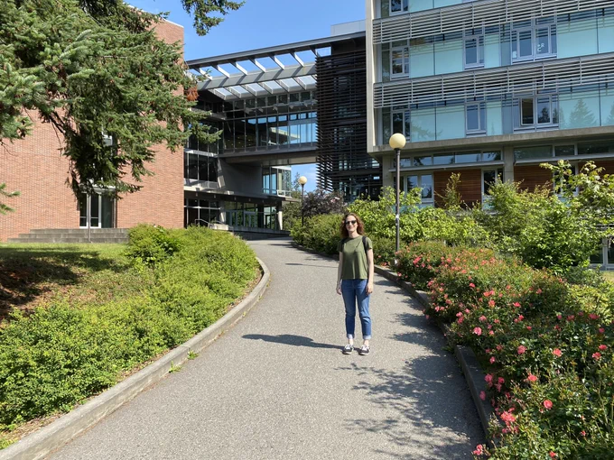 Sierra standing in front of a campus building with a curved path and green trees and flowers.