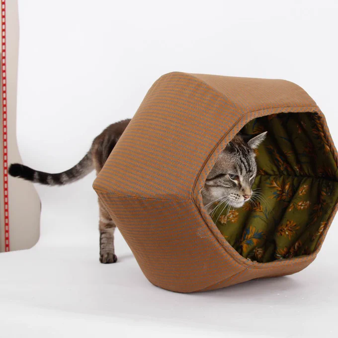 A large, very large, lynx point cat is walking g into a Cat Ball® cat bed from the smaller opening, so we can’t see his entire body. His face is partially visible in this cave-style cat bed, and the curve partially blocks view of his body, so only one rear foot and his long, striped tail are visible.