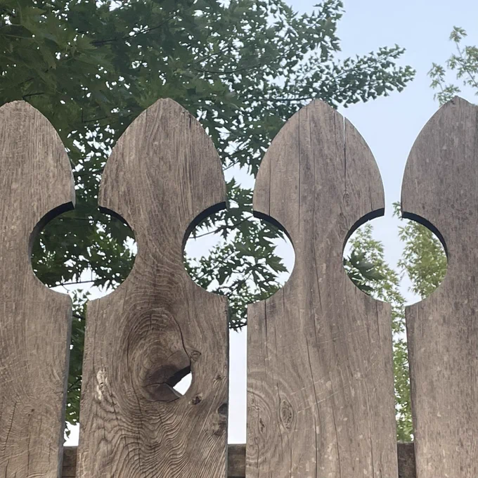 A fence with curves at the top of each post that create circles of negative space between them.