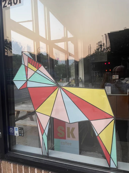 A painted Swedish Dalecarlian horse made of pink, sky blue, yellow, sea foam, and red triangles on the window of SK Coffee.