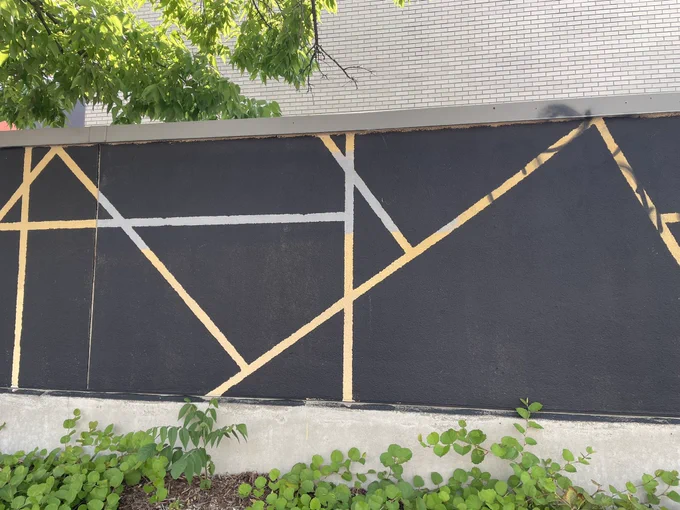 A wall painted black, cut into triangles, quadrilaterals, and pentagons by thick yellow and gray lines.