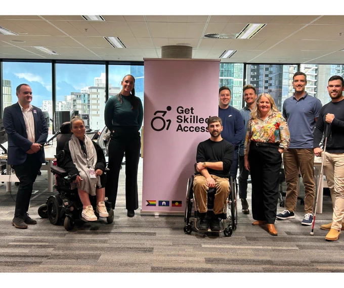 Get Skilled Access and Sport4All team are smiling and posing for a group photo in front of Get Skilled Access banner. 